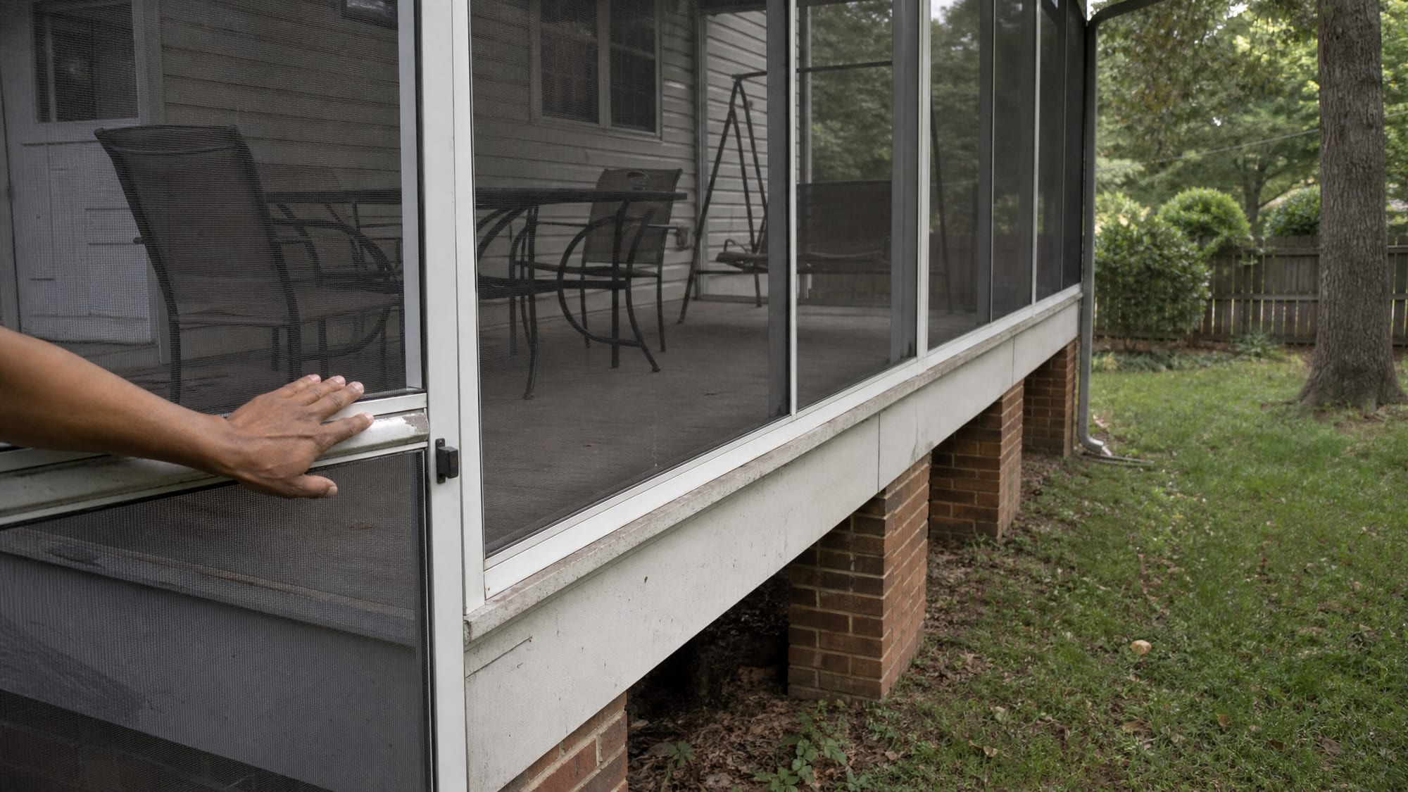 An existing screened-in back porch on a North Carolina home, standing on an open brick-pier foundation with the gap beneath the porch floor visible, in flat overcast afternoon light.