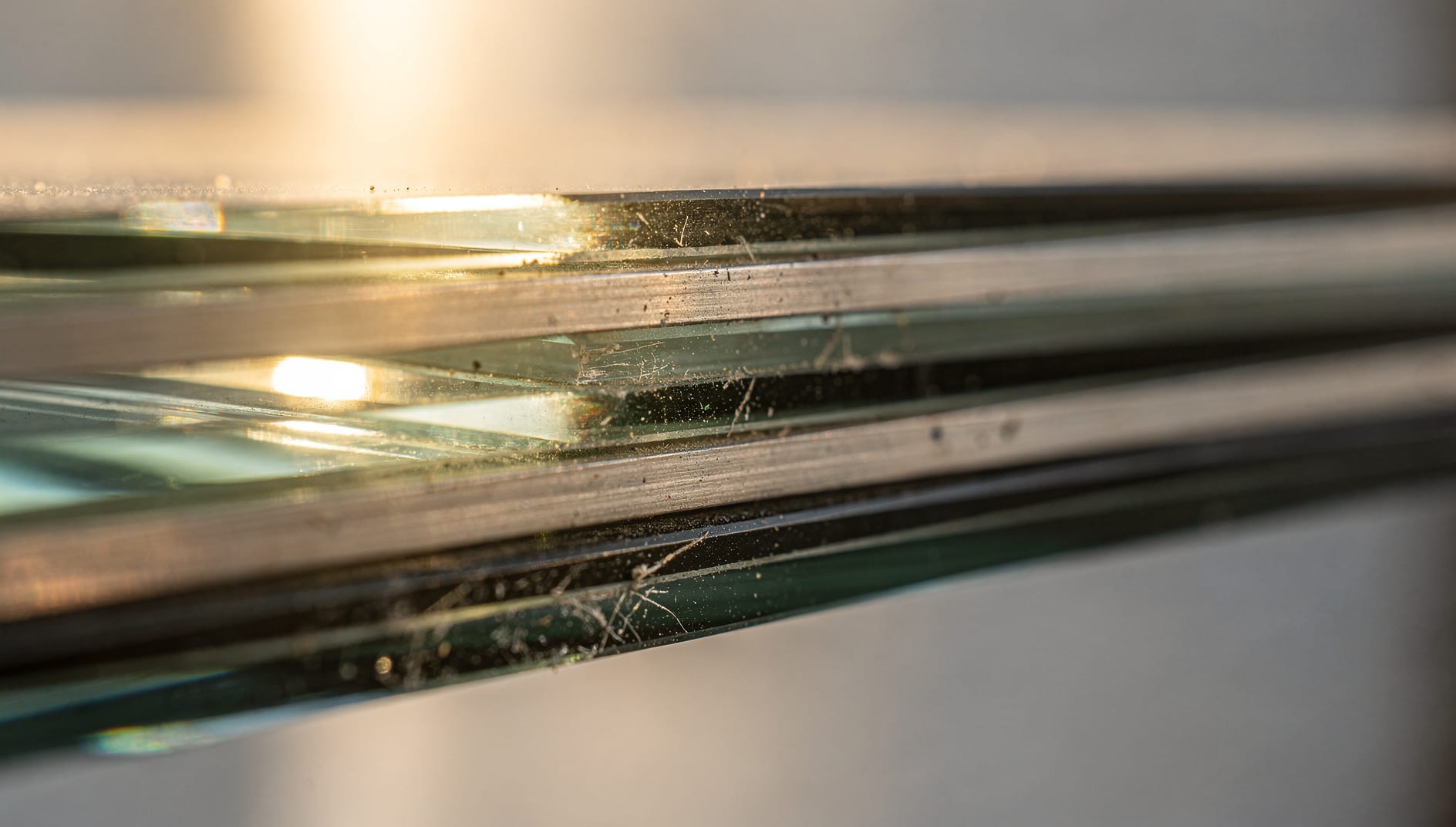 An extreme close-up of warm sunlight refracting through the layered panes and spacer bar at the edge of a multi-pane insulated glass window unit.