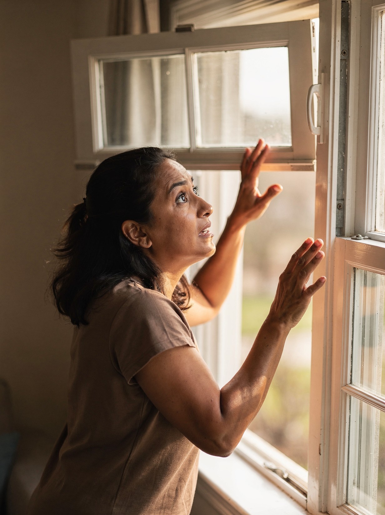 A woman flinches back from a double-hung window that has just slammed shut, one hand still raised mid-recoil, a startled and exasperated look on her face.